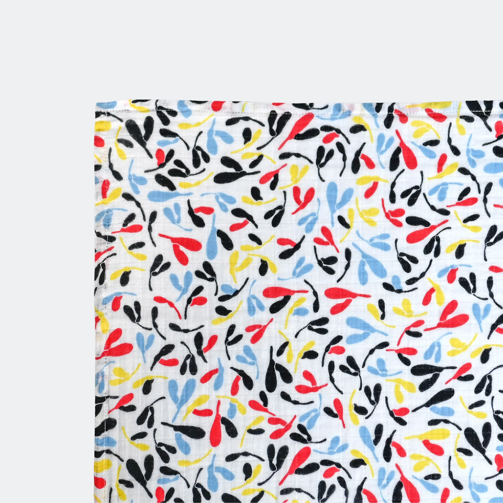 Fabric with a playful, colorful pattern of abstract leaves in red, yellow, blue, and black on a white background, conveying a lively, cheerful tone.