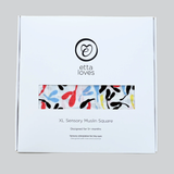 White Etta Loves box for XL Sensory Muslin Square with a window showing colorful pattern fabric.