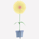 A stand-up paper flower decoration with yellow petals, a pink center, and a blue base stand.
