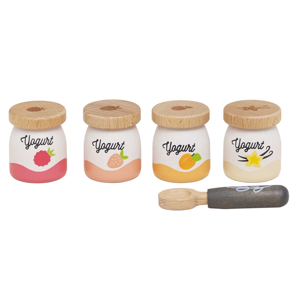 Four small wooden yogurt jars with fruit designs—raspberry, strawberry, peach, vanilla—each with a wooden lid. A wooden spoon lies nearby.