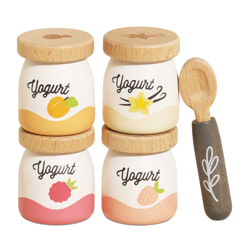 Four wooden yogurt jars with fruit illustrations—apricot, vanilla, raspberry, and strawberry—stacked in two columns, next to a wooden spoon.