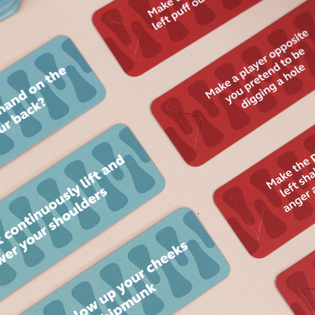 Red and blue party game cards with printed action prompts on a light surface.