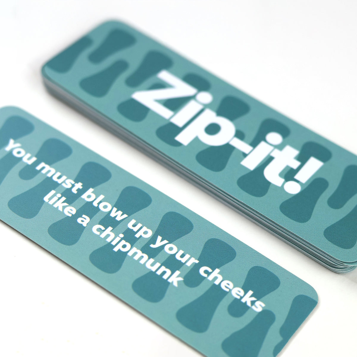 Teal Zip-it! party game cards, one reading "You must blow up your cheeks like a chipmunk"