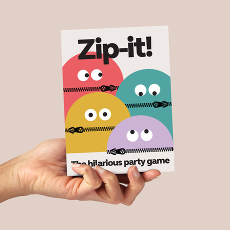A hand holds the "Zip-it! The hilarious party game" box featuring cartoon characters with zippered mouths.