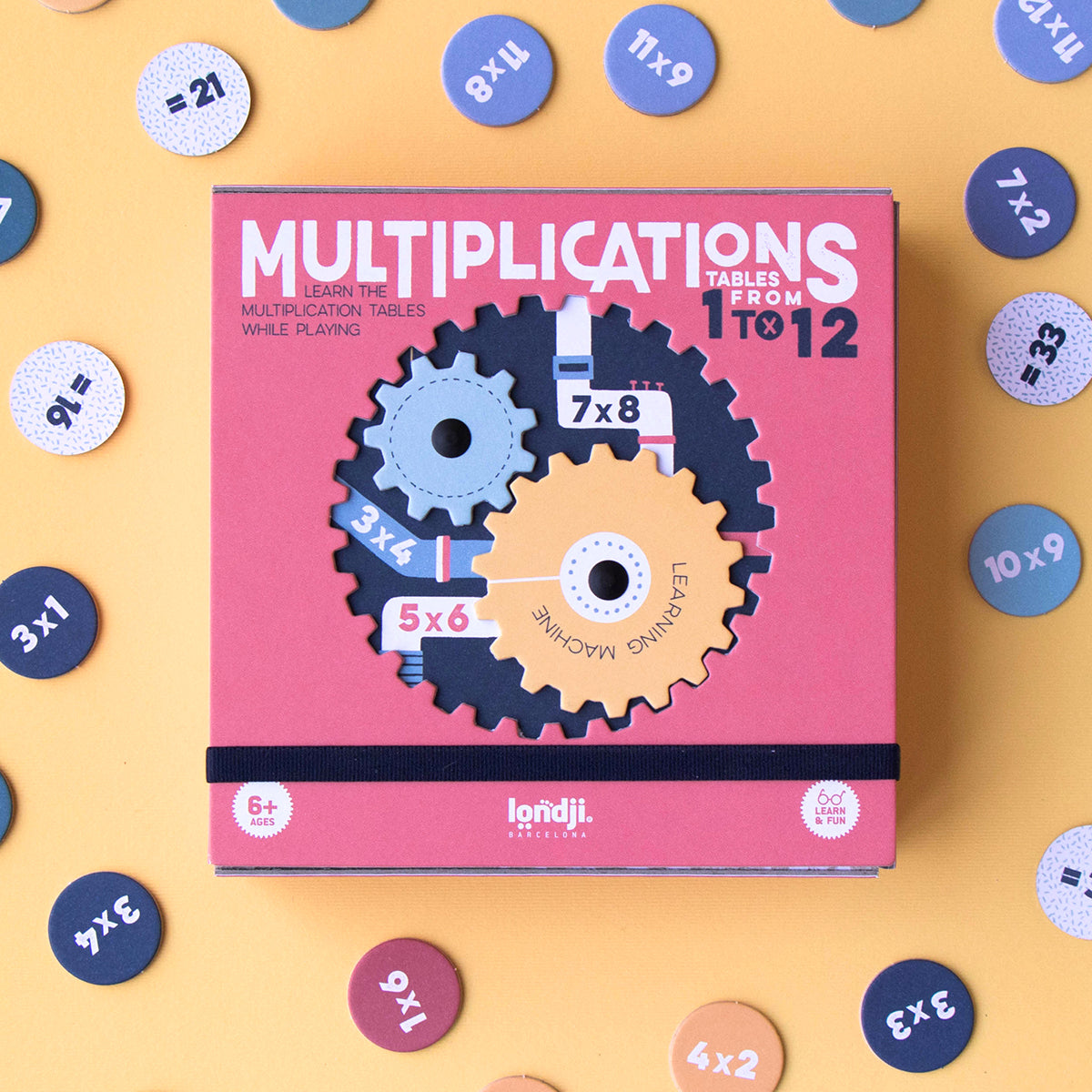 A box of the 'Multiplication Learning Machine' game with visible cogs and number discs, placed on a yellow background.