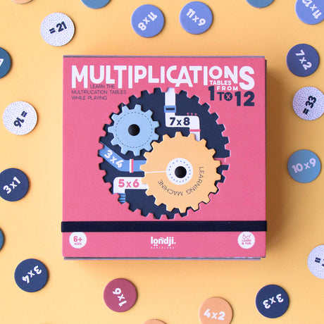 A box of the 'Multiplication Learning Machine' game with visible cogs and number discs, placed on a yellow background.