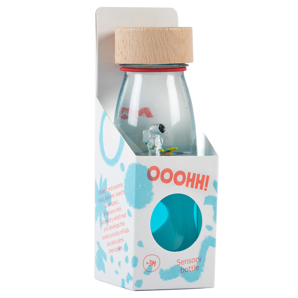 A Petit Boum astronaut-themed sensory bottle in its packaging, featuring a wooden cap and blue liquid with floating space-themed decorations.
