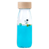 A clear sensory bottle with a wooden cap, filled with blue liquid, a floating astronaut figurine, and silver star-shaped confetti.